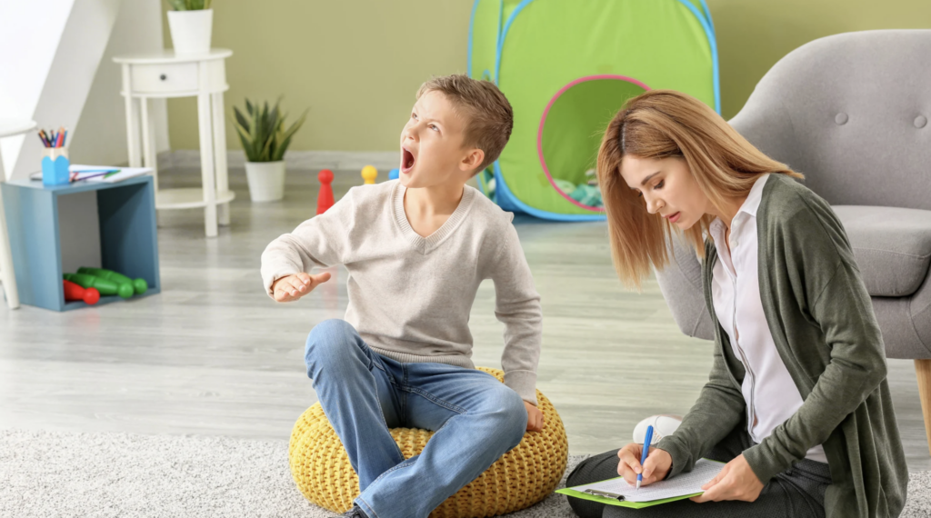 Child expressing frustration while sitting on a yellow pouf, with a woman taking notes nearby, in a bright room designed for family activities, reflecting themes of guardianship and support for children with disabilities in Texas.